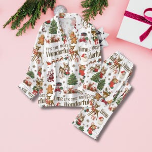 Op de afbeelding: Witte kerstpyjamaset met een overhemd met knopen en een bijpassende broek. De set heeft rendieren, peperkoekenmannetjes, kerstbomen en de tekst "It's the Most Wonderful Time". Feestelijke en gezellige nachtkleding.