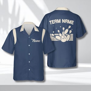 Puede incluir: Camisa de bolos azul marino con detalles crema en el cuello y las mangas. La parte delantera de la camisa tiene la palabra "Name" en cursiva. La parte trasera presenta "TEAM NAME" sobre un gráfico de bolos y bola.