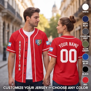 Puede incluir: Una camiseta de béisbol roja con ribetes blancos, cierre de botones y el texto ARGENTINA vertical en el pecho. El pecho izquierdo muestra un escudo ARG, con una bandera de Argentina en cada manga. La parte posterior muestra YOUR NAME y 00.
