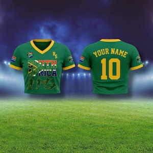 Puede incluir: Camiseta de f&uacute;tbol verde con ribetes amarillos y el texto "SOUTH AFRICA" en la parte delantera. La camiseta tiene la bandera de Sud&aacute;frica en las mangas y un cuello en V. La parte trasera de la camiseta tiene "YOUR NAME" sobre el n&uacute;mero "10".