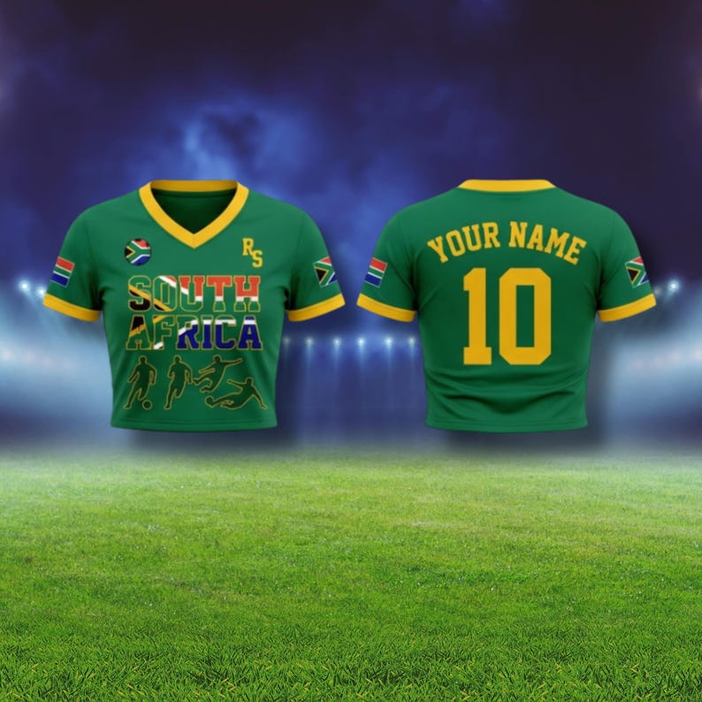 Puede incluir: Camiseta de f&uacute;tbol verde con ribetes amarillos y el texto "SOUTH AFRICA" en la parte delantera. La camiseta tiene la bandera de Sud&aacute;frica en las mangas y un cuello en V. La parte trasera de la camiseta tiene "YOUR NAME" sobre el n&uacute;mero "10".