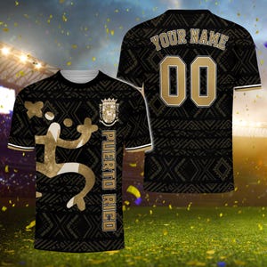 May include: Black and gold soccer jersey with a geometric pattern. The front features a gold figure, a crest, and the text "PUERTO RICO." The back displays "YOUR NAME" and the number "00" in gold.
