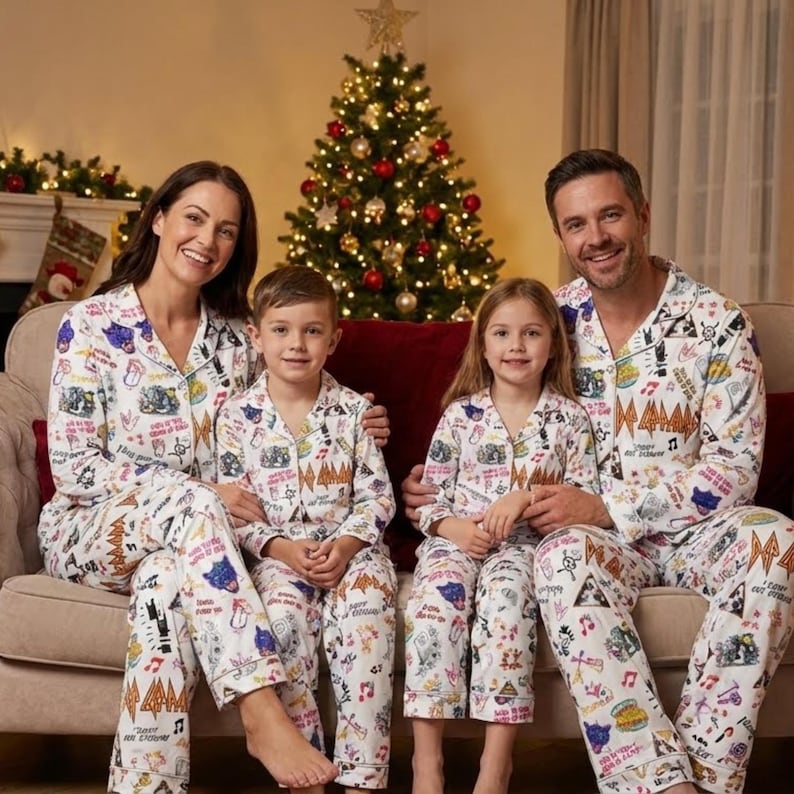 May include: A family of four wearing matching white pajamas with a colorful music-themed print. They are sitting on a beige couch in front of a decorated Christmas tree. The pajamas have a button-down top and pants.