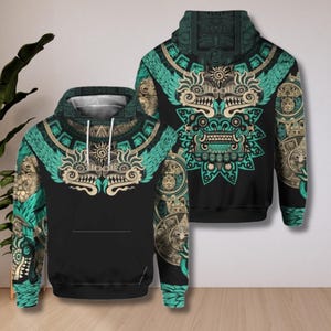 Op de afbeelding: Zwarte hoodie met een turquoise en beige Azteekse geïnspireerde design. Het ontwerp heeft een centraal zonachtig embleem met vleugels, omringd door ingewikkelde patronen en symbolen. De hoodie heeft een voorzak en een capuchon.
