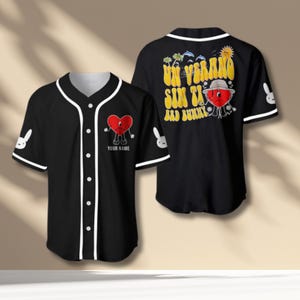 Könnte beinhalten: Schwarzes Baseball-Trikot mit weißem Besatz und Knöpfen. Verfügt über eine rote Herzfigur auf der Vorder- und Rückseite mit dem Text "Un Verano Sin Ti Bad Bunny". Enthält ein anpassbares Textfeld "Your Name". Weißes Hasenlogo auf den Ärmeln.