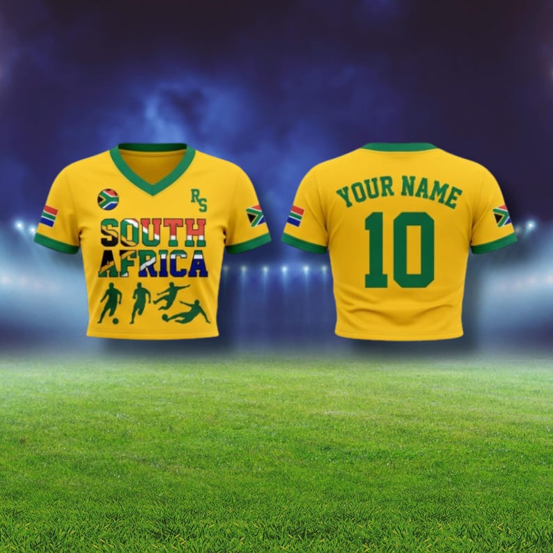Puede incluir: Camiseta de f&uacute;tbol amarilla con ribetes verdes y el texto "SOUTH AFRICA" en varios colores. La camiseta tiene el n&uacute;mero 10 en la espalda y las palabras "YOUR NAME" encima. Banderas sudafricanas en las mangas.