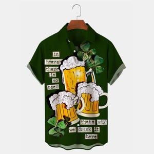 May include: Green short-sleeved shirt with a beer graphic. The design shows three beer mugs with frothy heads, shamrocks, and the text "in heaven there is no beer, that's why we drink it here."