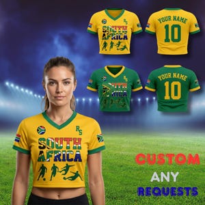 Puede incluir: Una camiseta de f&uacute;tbol amarilla y verde de Sud&aacute;frica con el texto "SOUTH AFRICA" y siluetas de jugadores de f&uacute;tbol. La camiseta tiene cuello en V y la bandera sudafricana en la manga. La imagen tambi&eacute;n muestra una camiseta verde.