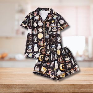 May include: Black pajama set with a whimsical print featuring potion bottles, moons, stars, and other magical elements. The short-sleeved top and shorts have gold trim. The fabric is a soft, lightweight material.