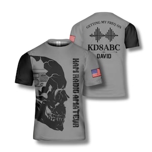 Könnte beinhalten: Graues T-Shirt mit schwarzen Ärmeln, mit einem Totenkopf-Design und dem Text "HAM RADIO AMATEUR". Auf der Rückseite steht "GETTING MY FREQ ON", eine Grafik und "KD8ABC DAVID". Enthält amerikanische Flaggen.