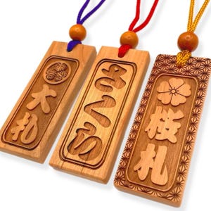 May include: Three wooden keychains with different designs. The first keychain has a Japanese character and a floral design. The second keychain has a Japanese character and a floral design. The third keychain has a Japanese character and a floral design.