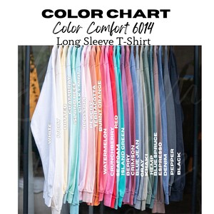 May include: A color chart of long sleeve t-shirts in various colors, including white, ivory, red, and black. The text "Color Comfort 6014" and "Long Sleeve T-Shirt" are displayed at the top. Each shirt is hanging on a rack.