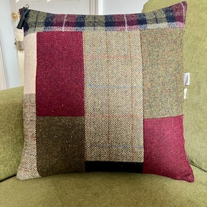 May include: A patchwork cushion cover with a mix of green, red, and beige tweed fabrics. The cushion cover has a zipper closure and a tassel.
