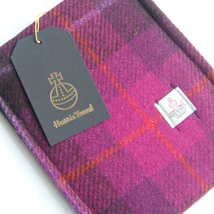May include: A pink, orange, and black plaid fabric swatch with a black tag that says "Harris Tweed" and a gold logo of a globe with a cross on top.