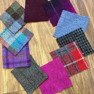 Puede incluir: Una colección de muestras de tela coloridas dispuestas sobre una superficie de madera. Las muestras presentan varios patrones, incluyendo cuadros, espiga y colores lisos en tonos de azul, morado, rojo y verde. Las muestras son cuadradas y tienen una apariencia texturizada.