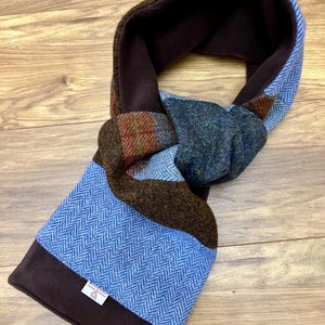 Könnte beinhalten: Ein brauner, blauer und roter karierter Schal mit braunem Fleece-Futter. Der Schal ist in der Mitte gefaltet und zu einem Knoten gebunden.