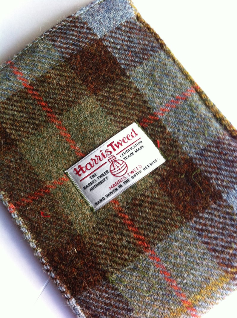 Może przedstawiać: Zbliżenie na brązową, zieloną i niebieską tkaninę tweedową z białą etykietą, na kt&oacute;rej widnieje napis "Harris Tweed, The Harris Tweed Authority Certification Trade Mark, Hand Woven in the Outer Hebrides".