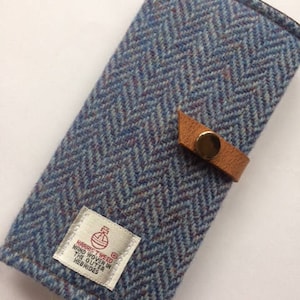 May include: A blue and brown tweed wallet with a leather strap and a label that reads "Harris Tweed Hand Woven in the Outer Hebrides".