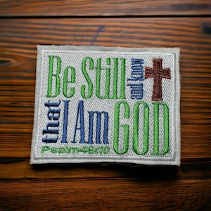 May include: White fabric patch with green, blue, and brown embroidery. The text reads "Be Still and Know that I Am God" with "Psalm 46:10" below.