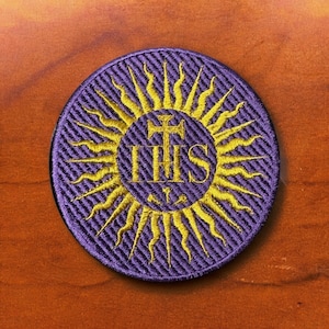 May include: Purple embroidered patch with a gold sunburst design and the letters "IHS" in the centre. The letters are surrounded by a cross and two keys.