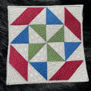 May include: A white square patch with a geometric design of red, green, and blue triangles. The patch is made of fabric and has a quilted texture.