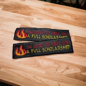以下が含まれることがあります： 赤い炎と「I'M GOING TO HELL ON A FULL SCHOLARSHIP」という文字が刺繍された黒いパッチが2つあります。