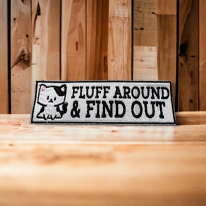 May include: A gray and white embroidered patch with a cartoon cat and the text "FLUFF AROUND & FIND OUT".