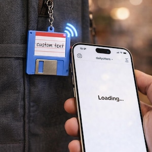 May include: A blue custom NFC tag in the shape of a floppy disk is attached to a backpack. The tag has the words "custom text" on it. A smartphone displays a loading screen, suggesting the tag is being read.