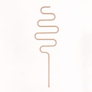 May include: A minimalist, abstract sculpture in a light peach color. The design features a straight, vertical stem that curves into a series of horizontal and vertical lines, creating a unique, flowing shape. The sculpture is set against a plain white background.