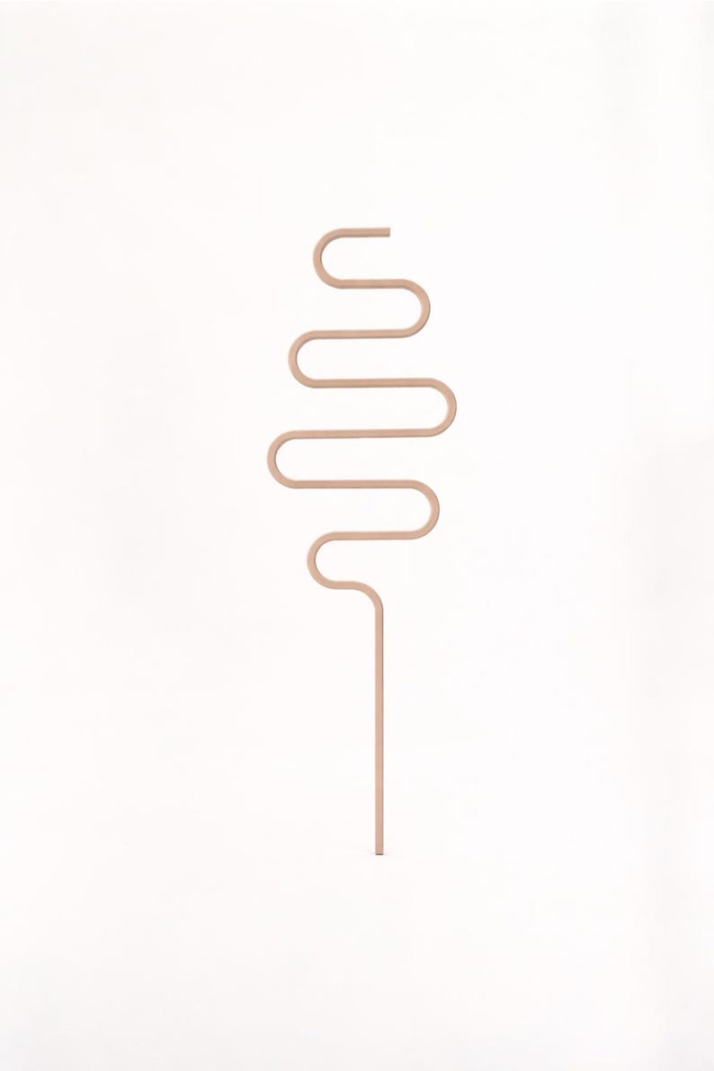 May include: A minimalist, abstract sculpture in a light peach color. The design features a straight, vertical stem that curves into a series of horizontal and vertical lines, creating a unique, flowing shape. The sculpture is set against a plain white background.
