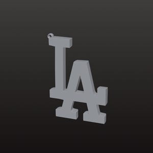 May include: A grey pendant displaying the interlocking "LA" logo, often linked to the Los Angeles Dodgers baseball team. The pendant is three-dimensional and has a small loop at the top for a chain. The background is a dark grey.