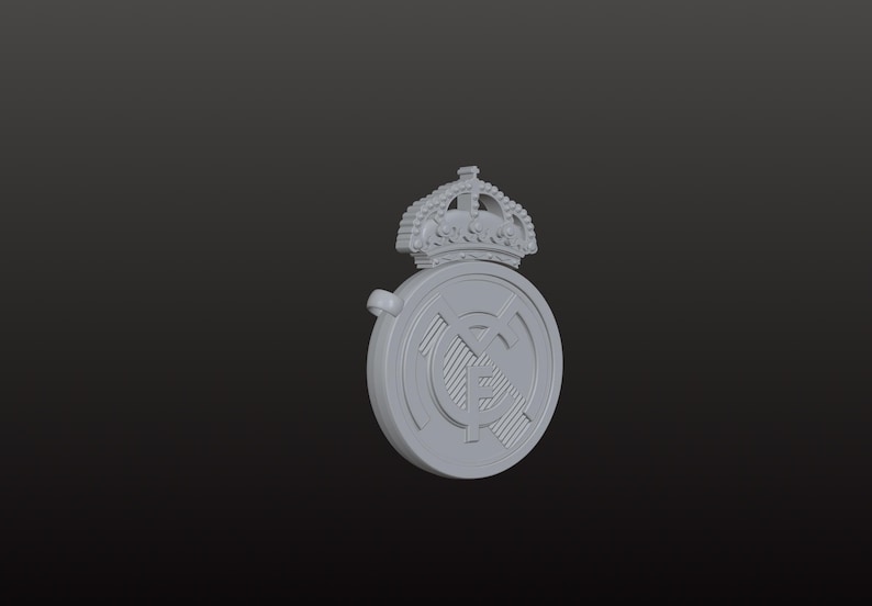 May include: A grey, three-dimensional emblem featuring a crown above a circular design. The circular design has a striped pattern and a smaller emblem in the centre. The emblem is set against a dark background.