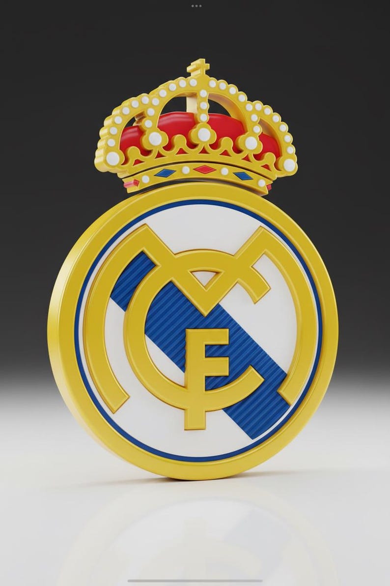 May include: A 3D render of the Real Madrid club crest. The emblem features a gold circle with a blue and white interior, and a gold crown at the top. The letters "M" and "F" are visible.