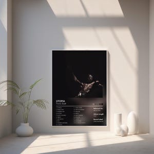May include: A framed poster for Travis Scott's album "Utopia." The poster features a dark image of a person with their arms raised. The album title and artist name are at the top, with a tracklist and release information below. The album length is 75:37.
