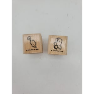 Op de afbeelding: Twee houten stempels met zwarte inktontwerpen. Eén stempel heeft een gestippelde vorm met een X in een cirkel, de andere heeft een hart en een cluster van stippen. Beide stempels hebben de tekst "Stampin' Up! 1996".