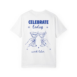 Puede incluir: Una camiseta blanca con un gráfico azul en la parte posterior. El diseño muestra dos manos sosteniendo copas de martini en un brindis, con el texto CELEBRATE today y work later, acentuado por pequeños símbolos de estrellas arriba y abajo.