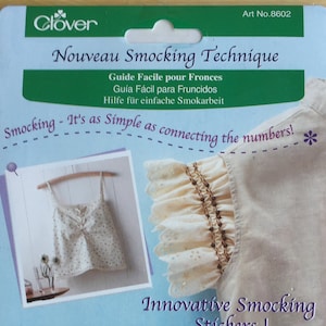 May include: A package of Clover Smocking Technique stickers. The package is green and white and features a photo of a white top with smocking on the sleeves. The text on the package reads "Nouveau Smocking Technique" and "It's as Simple as connecting the numbers!"