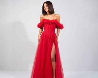 May include: A vibrant red off-the-shoulder gown with a high slit. The dress features a fitted bodice and a flowing skirt. The neckline is adorned with ruffled fabric, adding texture and detail to the elegant design.