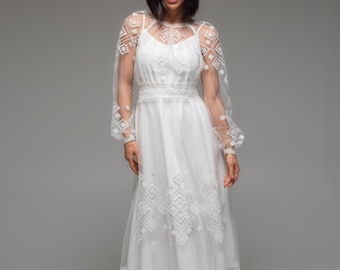 May include: White midi dress with geometric embroidery. The dress features a fitted bodice, spaghetti straps, and a sheer overlay with long, puffy sleeves. The skirt has a flared silhouette and is adorned with detailed embroidery.
