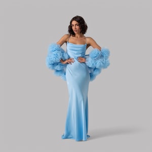May include: A woman wearing a light blue satin dress with a matching tulle shrug. The dress has a cowl neck and a fitted silhouette.