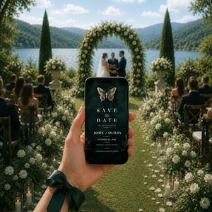 May include: A smartphone displaying a dark green digital Save the Date card featuring a gold butterfly graphic and the text Save the Date, John and Olivia, October 22, 2026. The phone is held against a backdrop of an outdoor wedding ceremony.