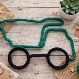 May include: A green and black yarn truck shape on a wooden surface, with craft supplies. The truck has black wheels and a green body. Other items include a succulent plant, twine, and small wooden stars. The truck is approximately 20 cm long.