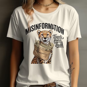 May include: Cream-colored t-shirt featuring a cheetah illustration carrying a bag labeled "FAKE NEWS." The shirt has the text "MISINFORMATION" above the cheetah and "Travels faster than Truth" below.