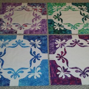 May include: Four square fabric quilt blocks with a white center and a floral design in the border. The blocks are in shades of purple, green, blue, and pink.
