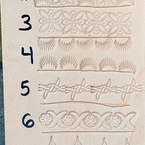 May include: A piece of light tan leather with eight different embossed border designs. The designs include floral patterns, sunbursts, and a barbed wire motif. The numbers 1 through 8 are written in black ink next to each design.
