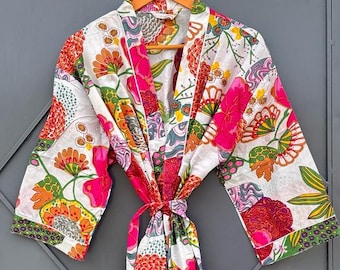 May include: A white floral print robe with a tie waist, featuring vibrant pink, orange, and green flowers. The robe is hanging on a wooden hanger against a gray door.