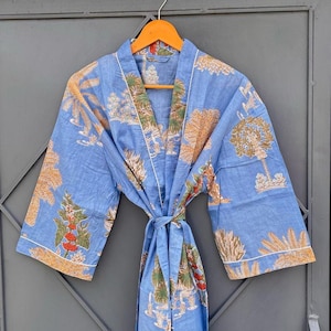 May include: A light blue robe featuring a repeating pattern of tan trees, green foliage, and red floral accents. The garment has wide sleeves, a wrap-front design with a matching fabric tie belt, and white piping along the collar and sleeve edges.