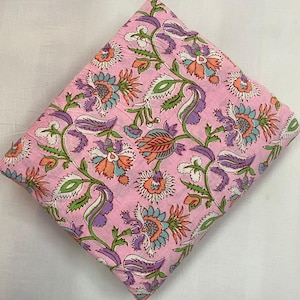 Könnte beinhalten: Ein gefaltetes Stück rosa Stoff mit einem floralen Muster. Das Design zeigt große Blüten in Orange, Lila und Blau, mit grünen Blättern und Stielen. Der Stoff ist wahrscheinlich Baumwolle oder ein ähnliches Material, geeignet zum Nähen oder Basteln.