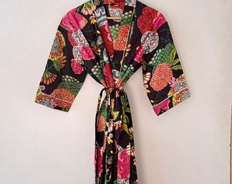 May include: A black floral print robe with pink, red, and green accents. The robe has a tie closure and white trim. It is hanging on a wooden hanger against a white wall.