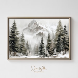 May include: A framed landscape print featuring a serene winter forest scene. The artwork depicts snow-covered trees and a mountain range shrouded in mist. The color palette is primarily muted tones of gray, white, and brown. The artist's signature and the name of the art print company are visible at the bottom.